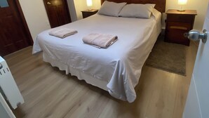 A neatly made bed with a wooden headboard, two bedside tables with lamps, and a wooden floor. - Spacious and comfortable house, excellent heating. (Punta Arenas)