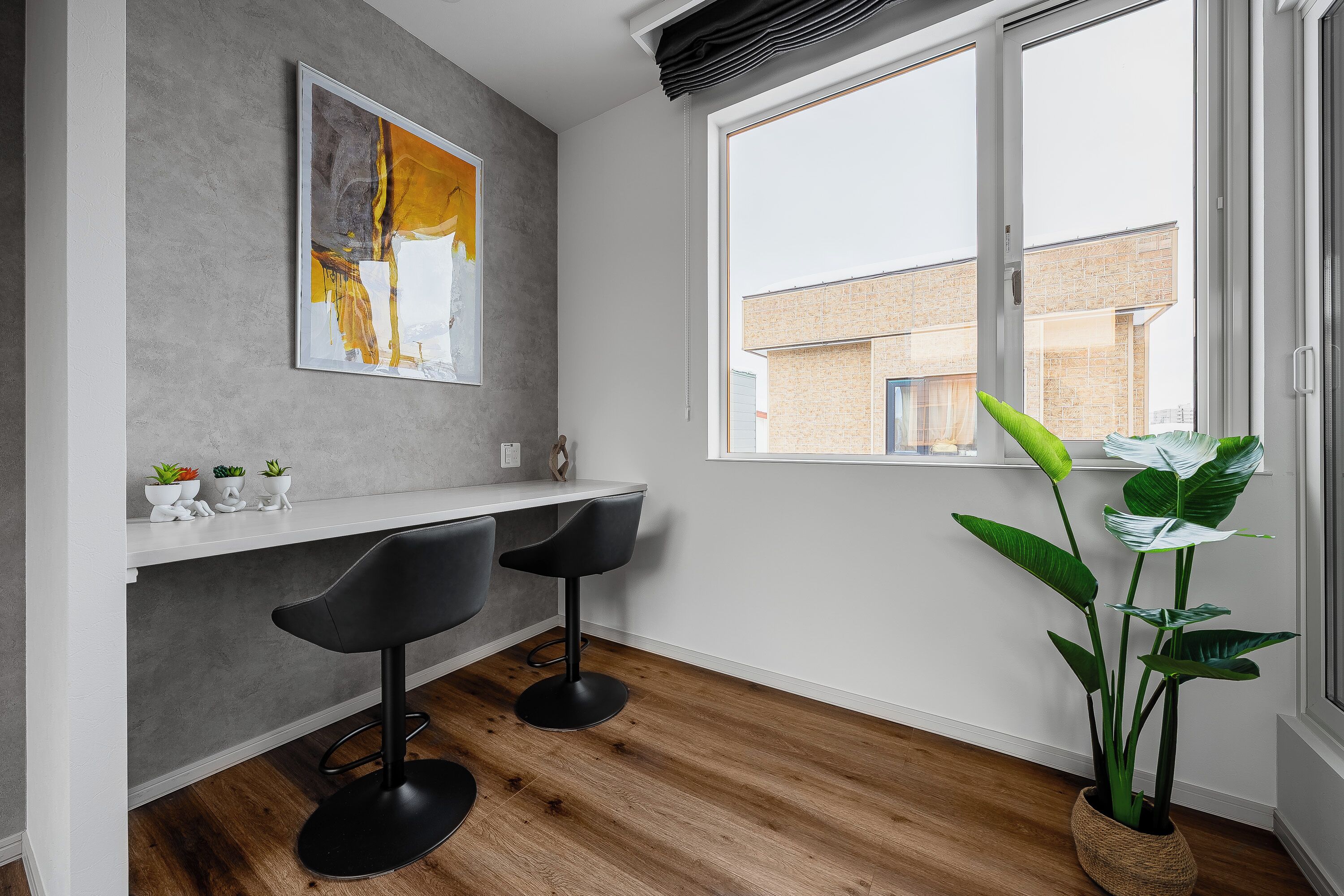 A modern kitchen with a large window, a painting on the wall, and two bar stools.