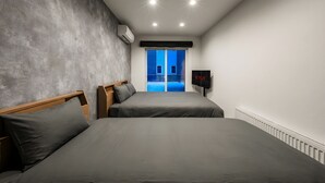 Ein Hotelzimmer mit zwei Betten, einem Fernseher und Blick auf ein blaues Gebäude.