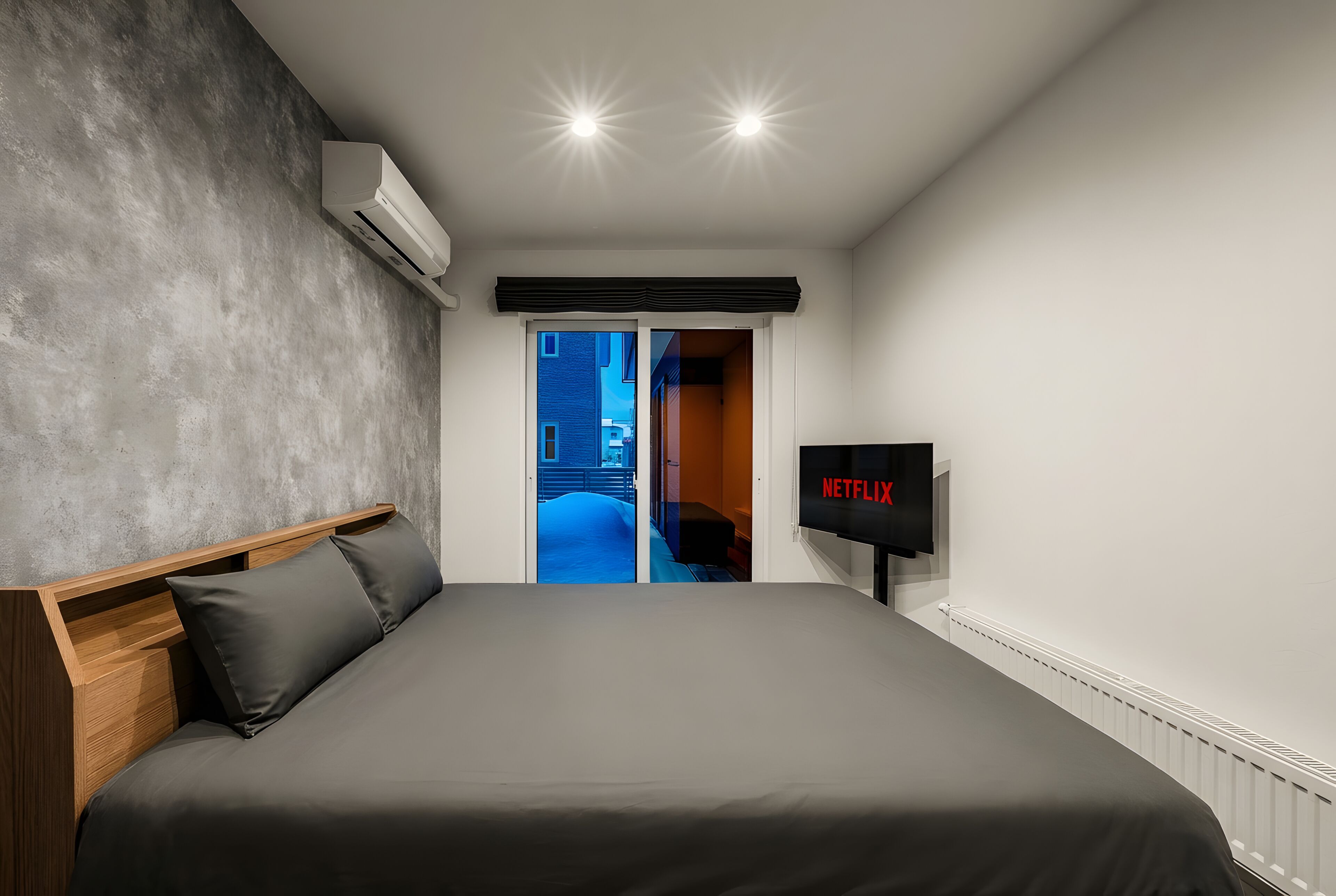 A modern bedroom with a large bed, a flat-screen TV, and an air conditioning unit.