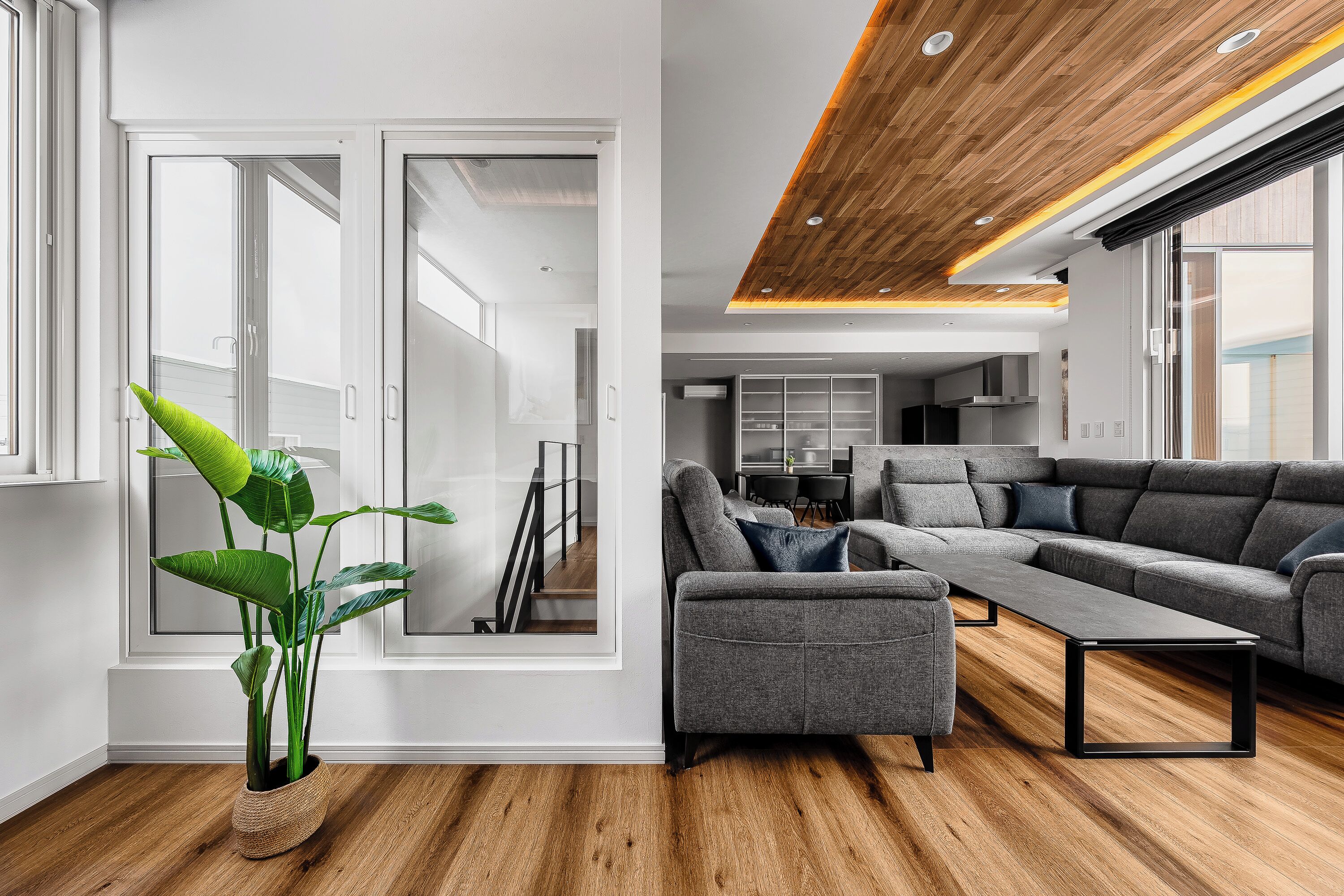 Una sala moderna con un sofá seccional gris, una mesita de centro y una planta verde grande.
