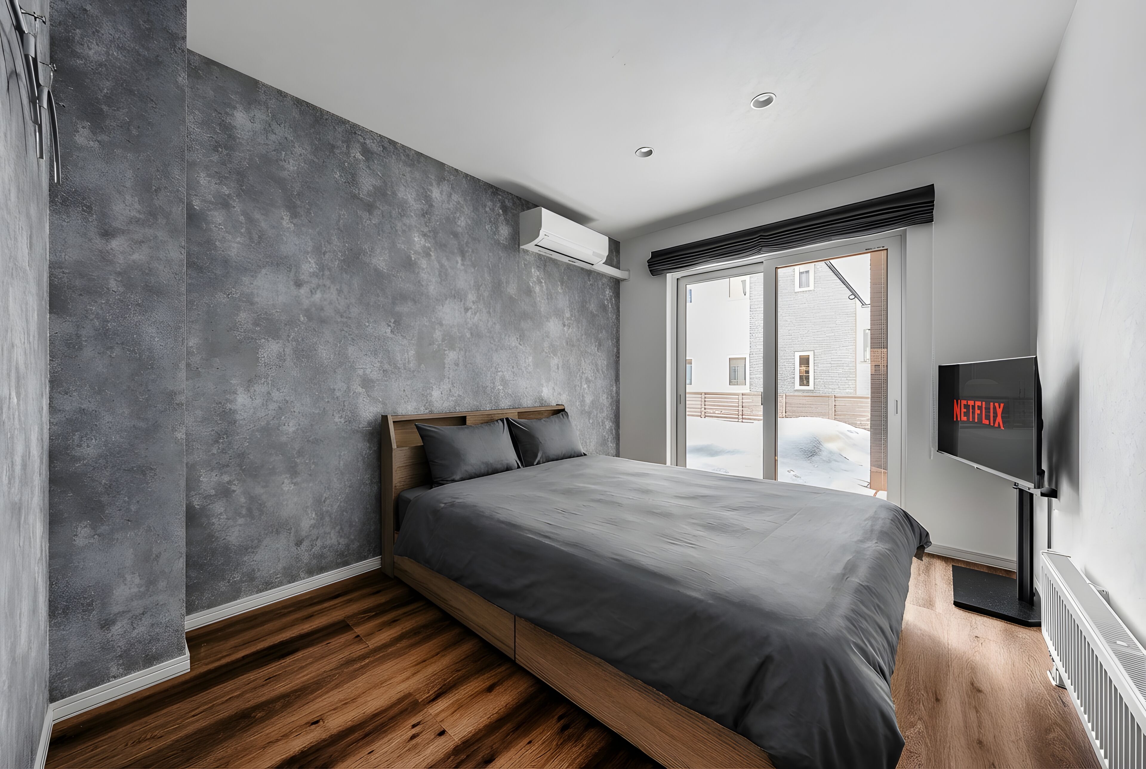 Un dormitorio moderno con cama, televisor y vistas al exterior.