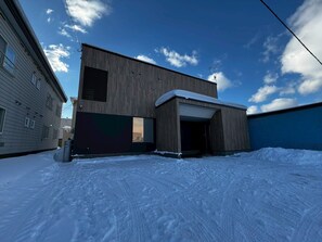 A modern building with a large garage door, a sloped roof, and a clear sky. - TDR Toti Design Room (Furano)