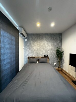 A modern bedroom with a large bed, a wall-mounted TV, and a potted plant. - TDR Toti Design Room (Furano)