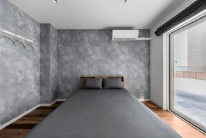 A modern bedroom with a large bed, grey walls, wooden flooring, and a window with a view.