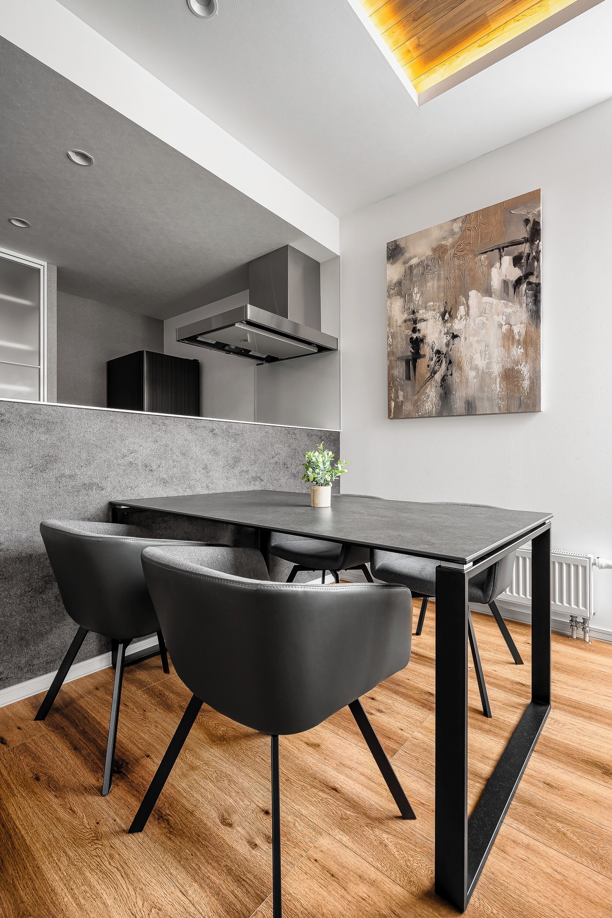 Un moderno comedor con una mesa y sillas negras, una planta en maceta y un cuadro abstracto grande en la pared.
