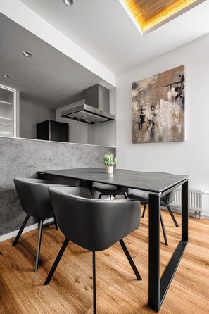 Un moderno comedor con una mesa y sillas negras, una planta en maceta y un cuadro abstracto grande en la pared.
