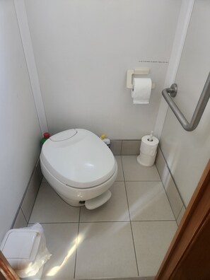 Une petite salle de bain propre, équipée de toilettes, d’un sèche-mains et d’un distributeur de serviettes en papier.