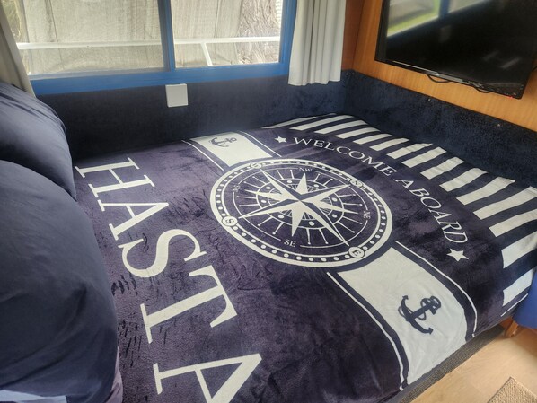 A bed with a nautical-themed bedspread featuring a compass and the words 'WELCOME ABOARD.'