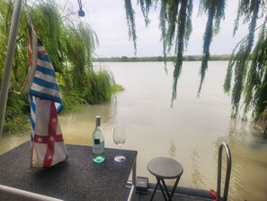 Un bateau avec une bouteille de vin et un verre sur le pont, entouré d’eau et de verdure.