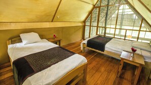 Una habitación acogedora con dos camas, piso de madera y ventanas amplias que dejan entrar luz natural.