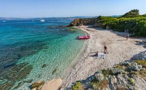 A beach with clear turquoise water, rocky terrain, and a few boats in the distance. - Upper Floor of Villa Delphine with Air Conditioning (SIX FOURS LES PLAGES)