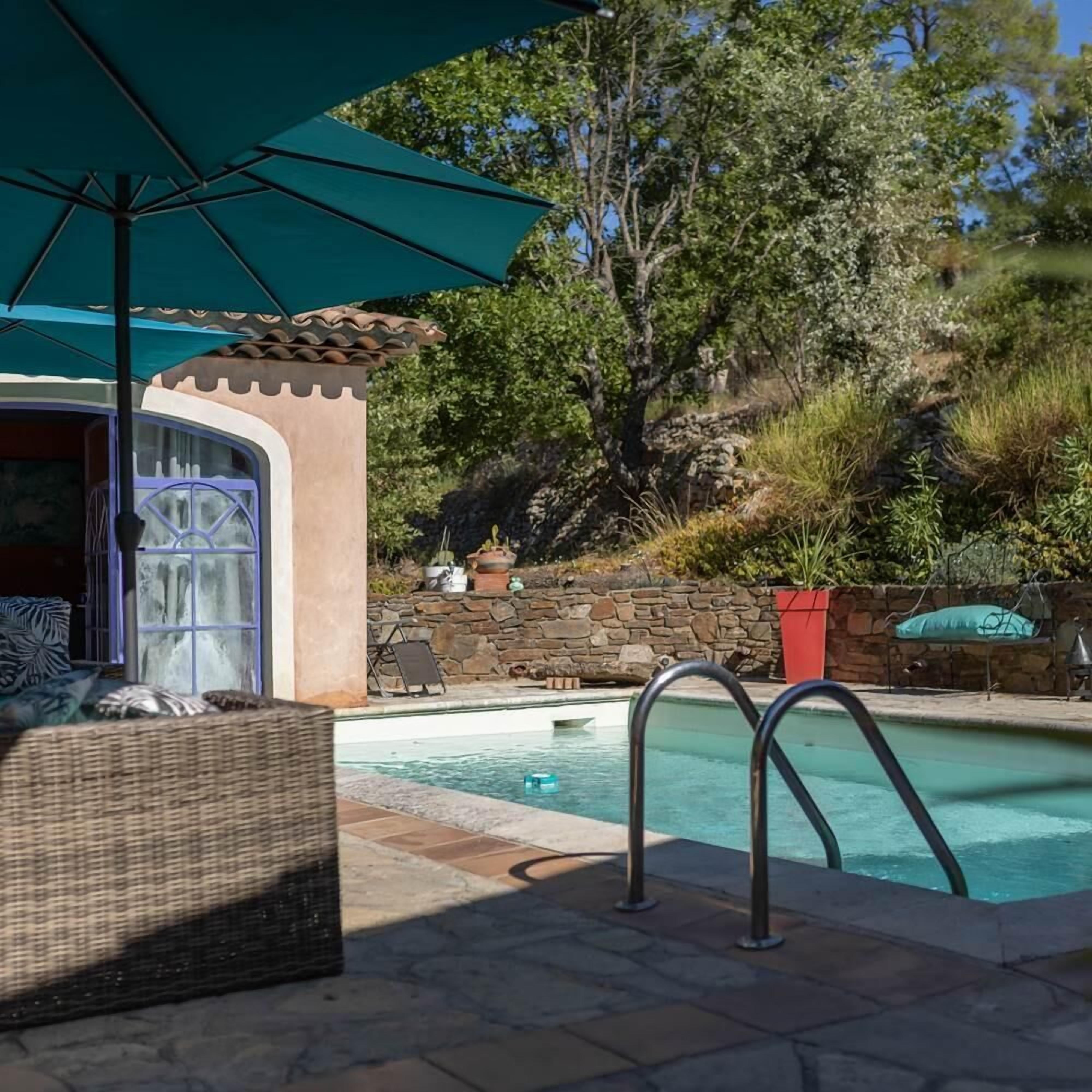 A pool area with a stone wall, a covered seating area, and a view of trees.