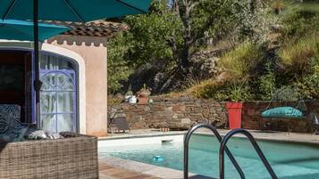 A pool area with a stone wall, a covered seating area, and a view of trees.