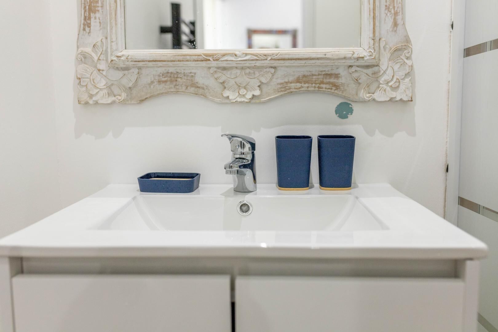 A white bathroom sink with a mirror, a faucet, and two blue cups.