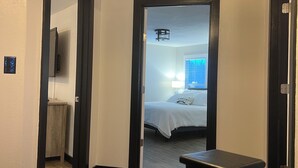 Ein Hotelzimmer mit Holzboden, einem Bett mit weißer Bettwäsche, einem Schreibtisch und einem Deckenventil.