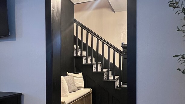 Ein Flur mit Holzboden, einer schwarzen Treppe und einer weißen Wand mit einem angebrachten Fernseher.