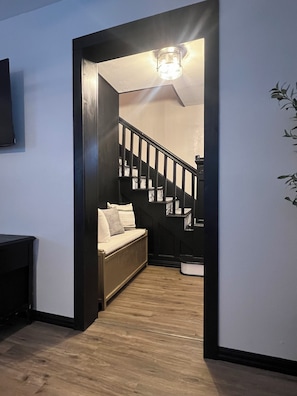 A hallway with a wooden floor, a black staircase, and a white wall with a mounted television.