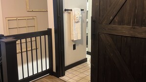 Ein Holzboden-Flur mit schwarzer Geländer, einer weißen Tür und Blick in ein Badezimmer mit Handtuch an einem Wäscheständer.