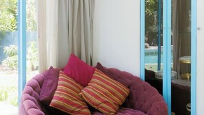 Une pièce dotée d’une grande fenêtre, d’un coin salon agrémenté de coussins violets et offrant une vue sur une piscine extérieure.