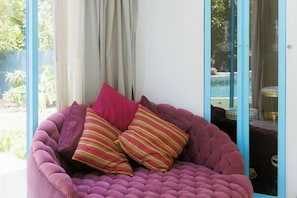 Una habitació amb una finestra gran, una zona de seients amb coixinets morats i vista a una piscina exterior.