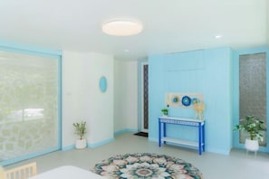 Una habitació amb un gran finestral, una taula rodona i un alfàbrega floral, un taulell blau i una planta en test.