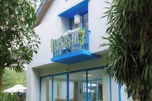 Un edificio con balcón adornado con flores, entrada de vidrio y detalles en azul.