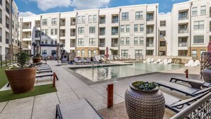 A modern hotel courtyard with a swimming pool, lounge chairs, and potted plants. - Luxury 1B w Pool near Legacy West (Frisco)