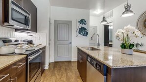 A modern kitchen with stainless steel appliances, a wooden floor, and a central island with a sink. - Luxury 1B w Pool near Legacy West (Frisco)