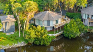 Una casa con veranda affacciata su un corpo d'acqua, circondata da vegetazione rigogliosa e alberi.
