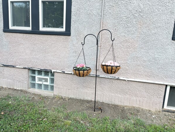 En byggnadsfasad med två hängande blomkorgar på ett metallstativ.