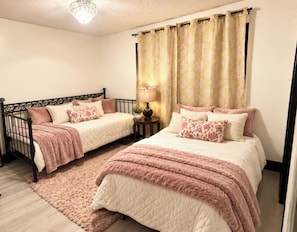 A bedroom with two beds, a chandelier, a lamp, and curtains.