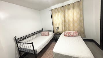 Quarto com duas camas de solteiro, uma mesa pequena e cortina.