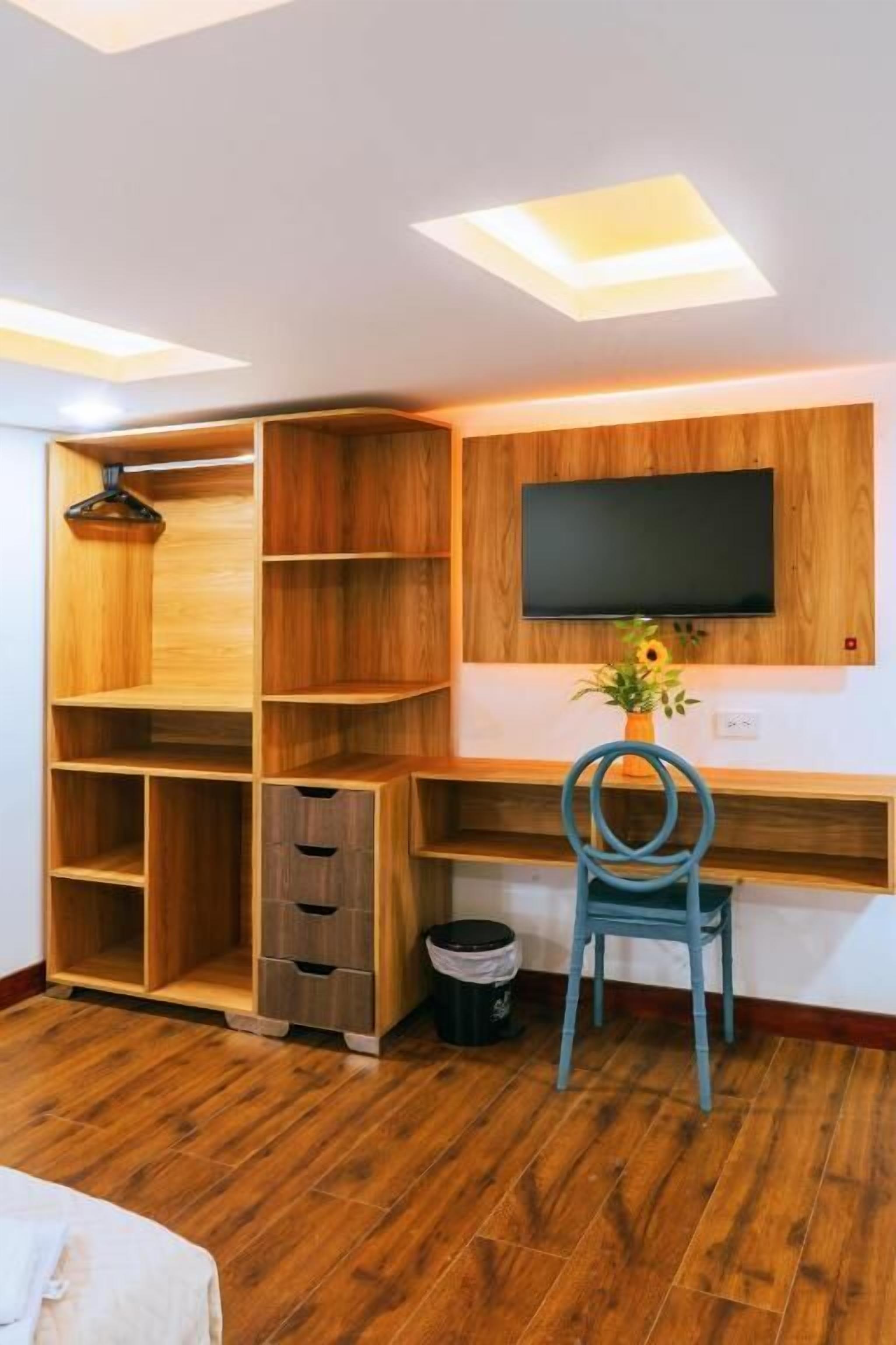 A room with a wooden desk, a chair, a TV mounted on the wall, and a ceiling light fixture.