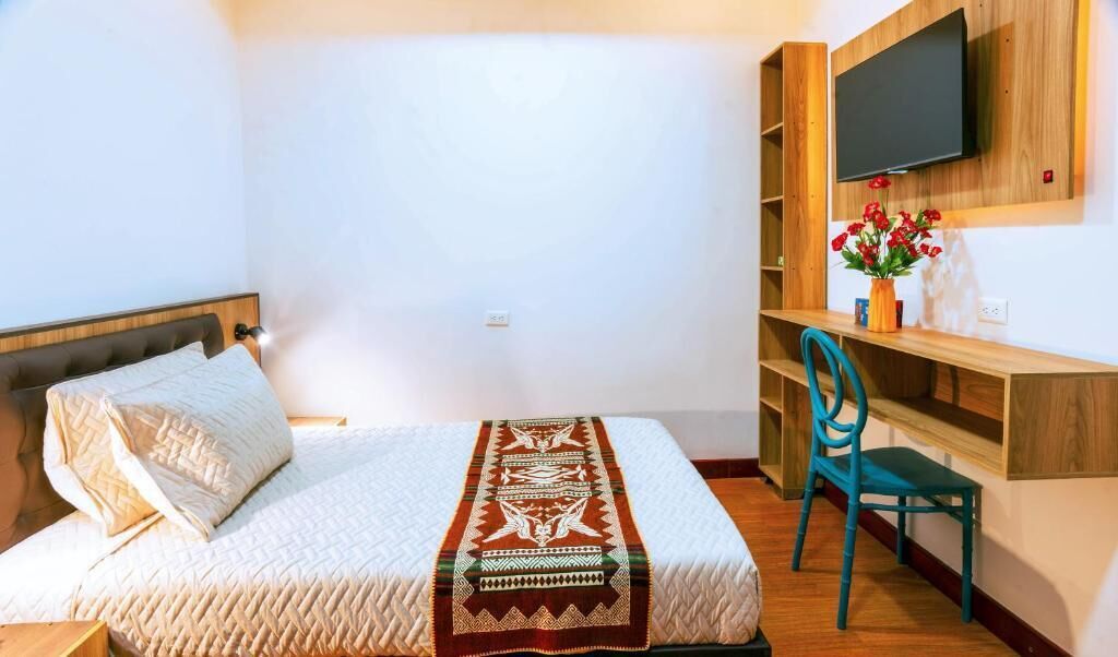 Un dormitorio con una cama, un escritorio, una silla y un televisor montado en la pared.