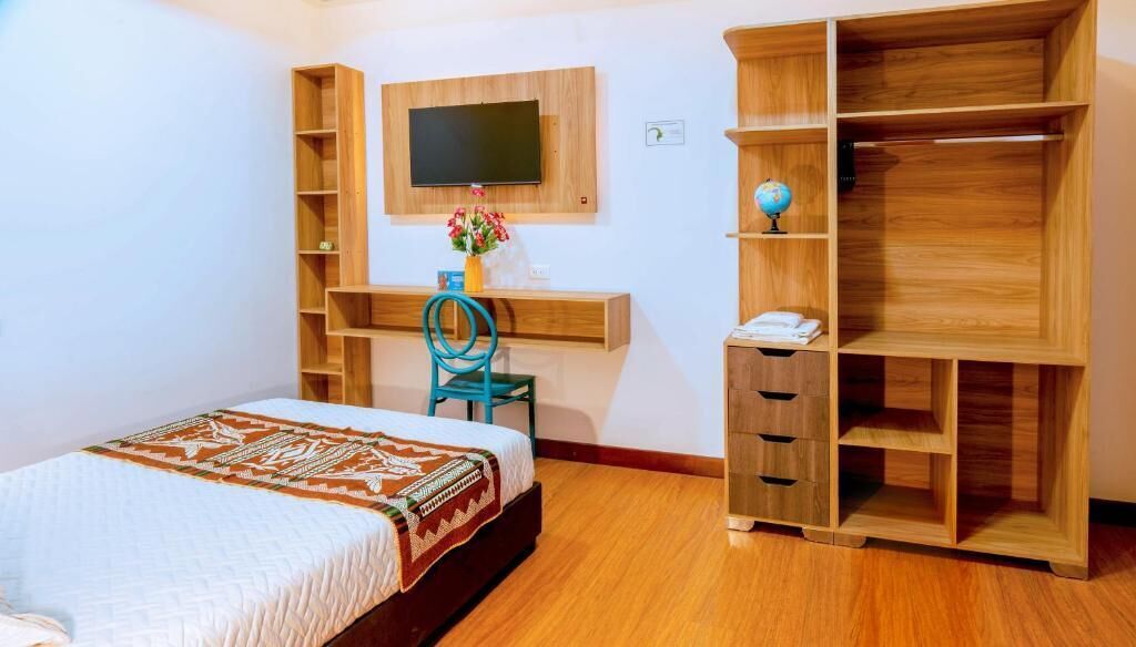 A bedroom with a bed, a desk, a chair, a TV, and built-in wooden shelves.