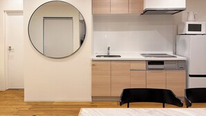 A modern kitchen with a round mirror, built-in cabinets, a microwave, and a sink. - b hotel Tekkyodo (Hiroshima)