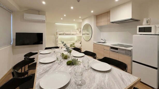 A modern kitchen with a built-in microwave, a sink, and a dining area with a marble table set for four. - b hotel Tekkyodo (Hiroshima)