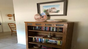 Ein Bücherregal aus Holz mit Büchern und Dekoration, ein gerahmtes Bild an der Wand und ein Stuhl im Hintergrund.
