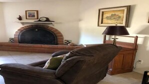 Ein Wohnzimmer mit Kamin aus Ziegelsteinen, einem braunen Ledersessel, einem Holzschrank und einer Lampe.