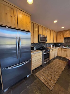 A modern kitchen with wooden cabinets, stainless steel appliances, a microwave, and a patterned rug.