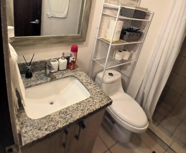 A bathroom with a granite countertop sink, a toilet, and a white shelving unit with toiletries. - Vista Tower, Apartamento 3 hab. piscina, gym, rooftop (San Salvador)