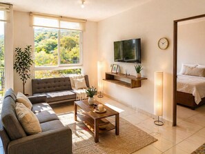 A modern living room with a sofa, coffee table, TV, and a bed in the adjacent room. - Vista Tower, Apartamento 3 hab. piscina, gym, rooftop (San Salvador)