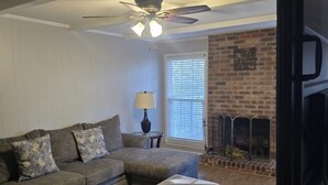 A living room with a sectional sofa, ottoman, ceiling fan, fireplace, and a TV on the wall. - Masters Week Golf Retreat-4BR Home on Golf Course (Augusta)