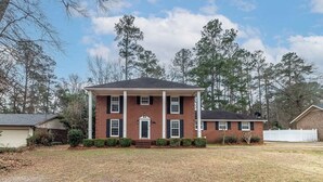A two-story brick house with a front porch, a garage, and a well-maintained lawn. - Masters Week Golf Retreat-4BR Home on Golf Course (Augusta)