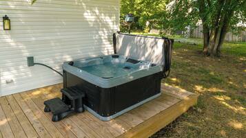 A hot tub on a wooden deck with a house in the background.