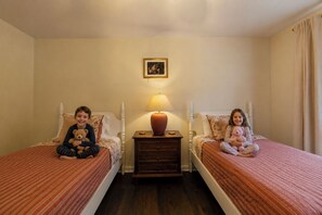 Deux lits jumeaux, séparés par une table de chevet sur laquelle se trouve une lampe, et un tableau encadré accroché au mur.