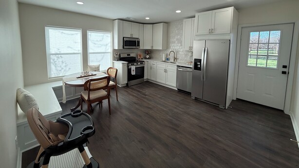 A modern kitchen with white cabinets, stainless steel appliances, and a dining area with a table and chairs. - Hot Tub- Sleeps 10- Bourbon Trail- Historic Home (Coxs Creek)