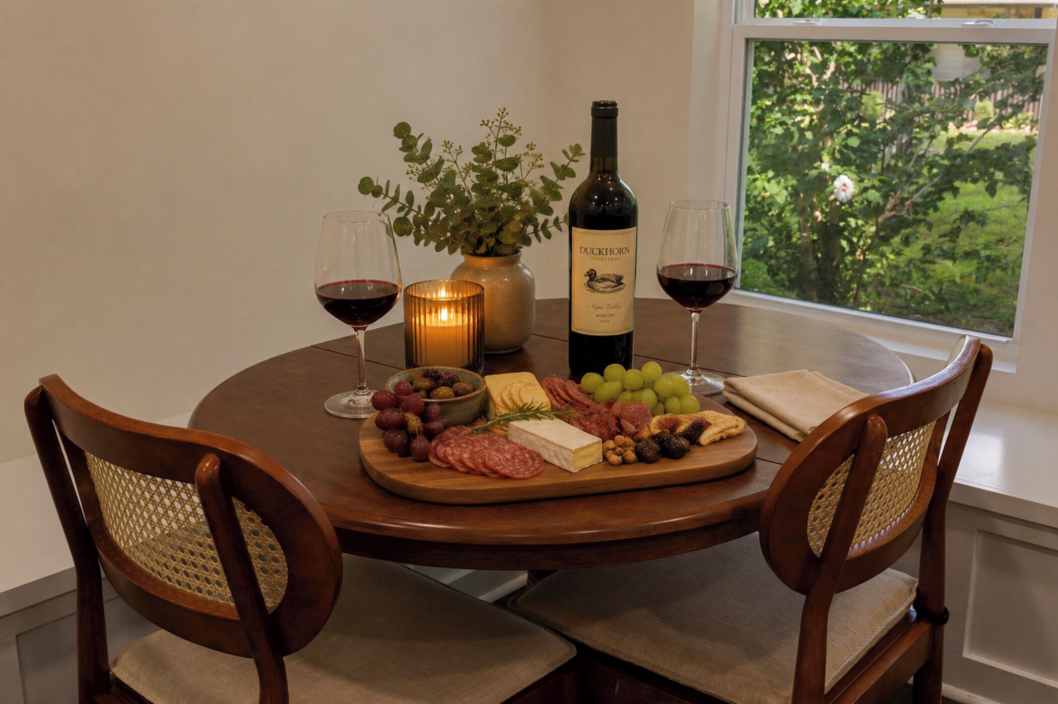 Et rundt spisebord med en flaske Duckhorn vin, glas, et stearinlys og et udvalg af oste samt charcuteri.