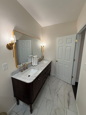 Un baño con tocador de doble lavabo, un espejo grande, apliques de pared y una puerta que da a otra habitación.